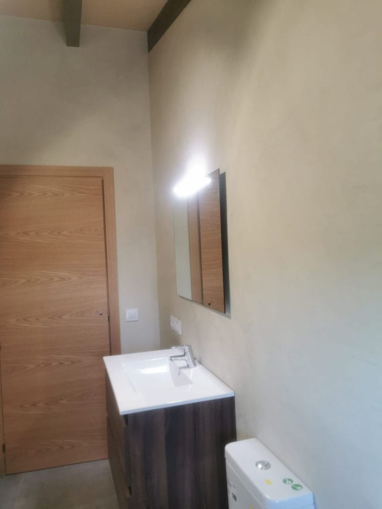 Bany amb revestiment de microciment i mobles de fusta natural.