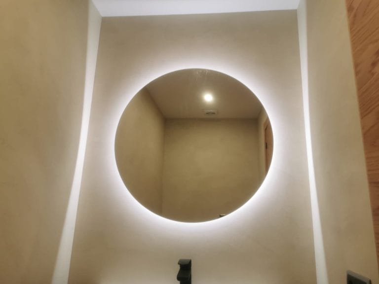 Bany modern amb parets de microciment i mirall rodó il·luminat.