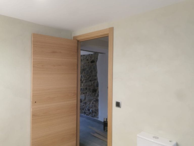 Entrada al bany amb porta de fusta i parets revestides amb microciment a Girona.