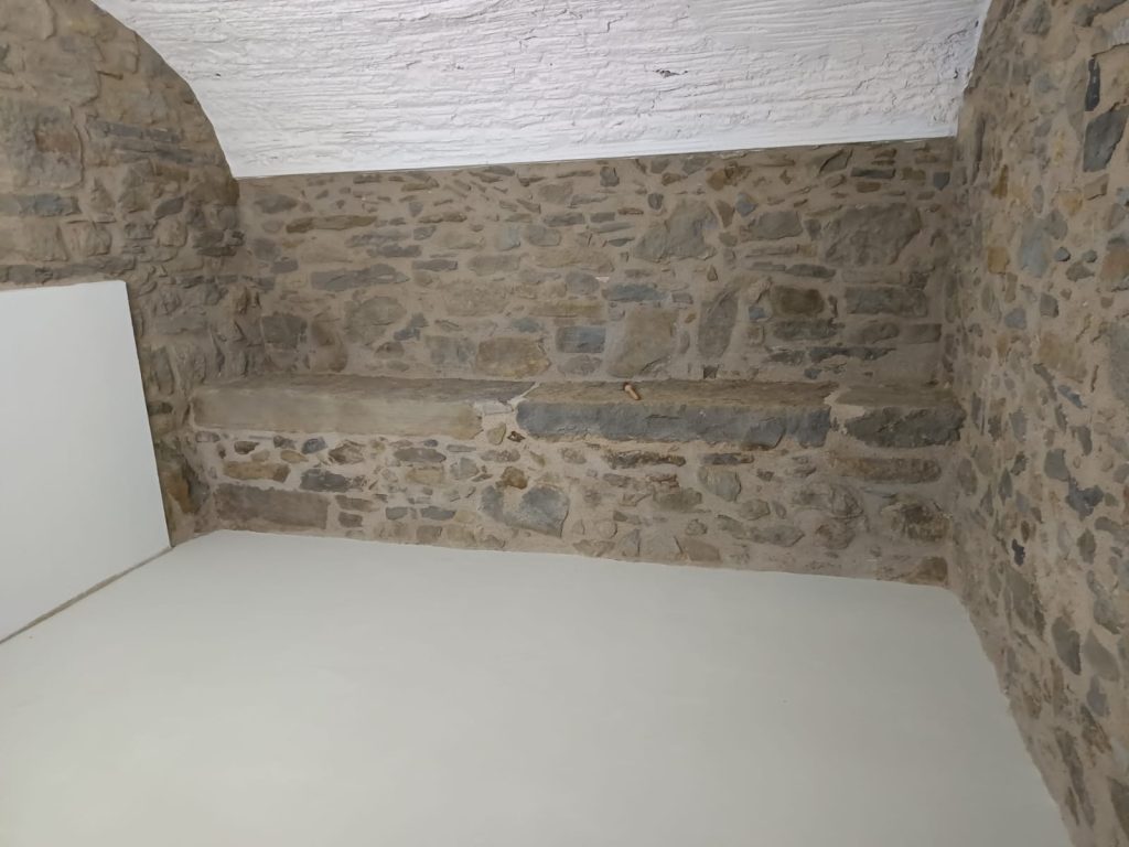 Espai amb parets de pedra natural i terra revestit amb microciment.