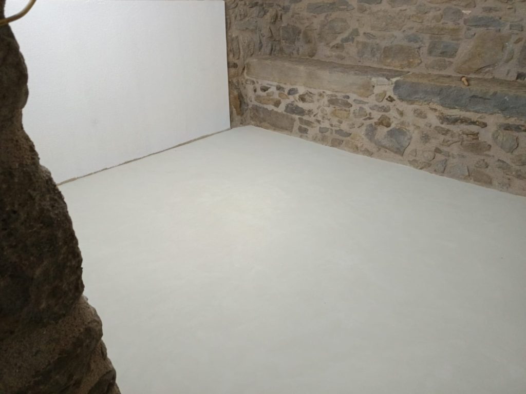 Habitació amb acabat de microciment en el terra i parets de pedra vista.
