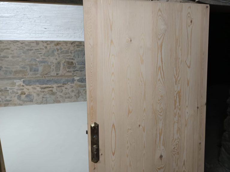 Entrada amb porta de fusta clara i terra de microciment resistent.